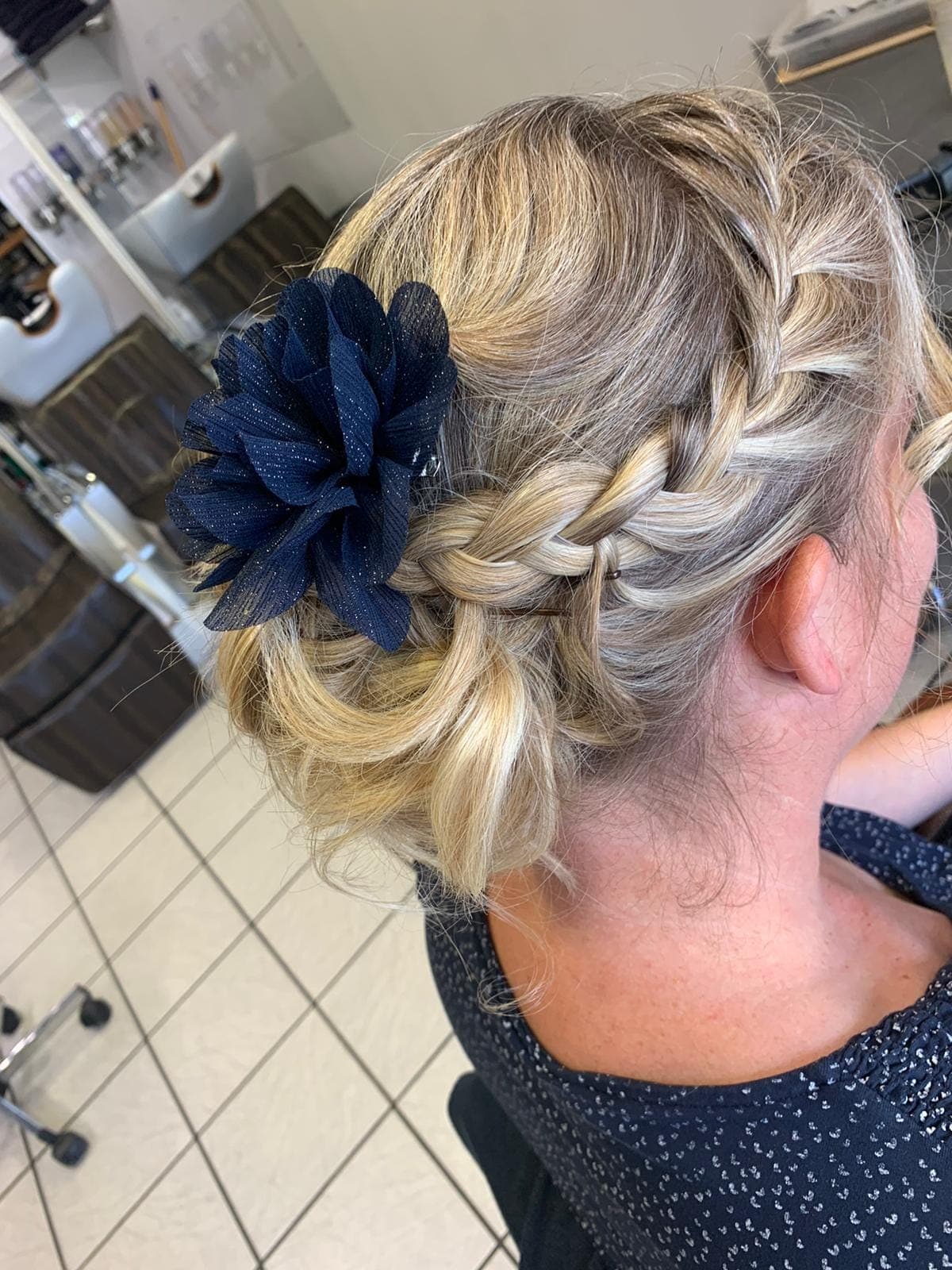 Chignon tressé rehaussé d'une fleur bleu marine, coiffure de cérémonie